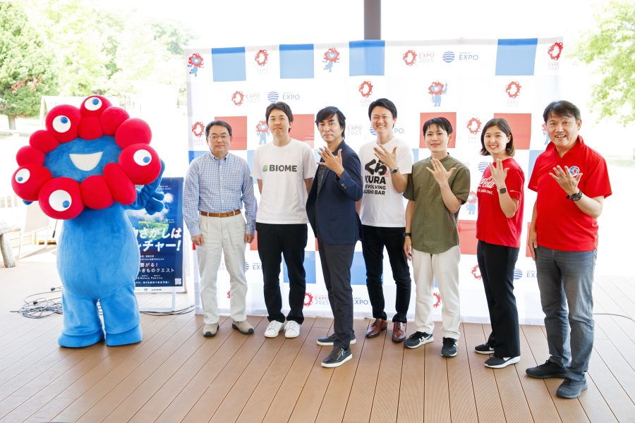 ウッドデッキの上に立つミャクミャクと7人のプロジェクトチーム
